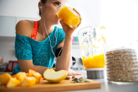Woman drinking an orange smoothie beside a blender